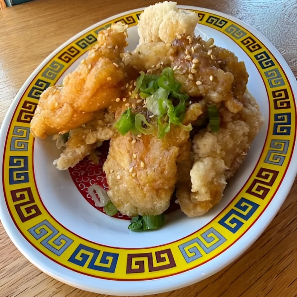 Crispy fried chicken karaage, garnished with sesame seeds and green onions, on a decorative plate.