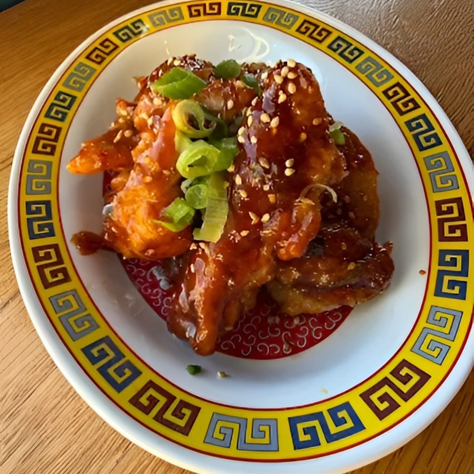 Sweet and sour chicken with sesame seeds and green onions on a decorative plate.