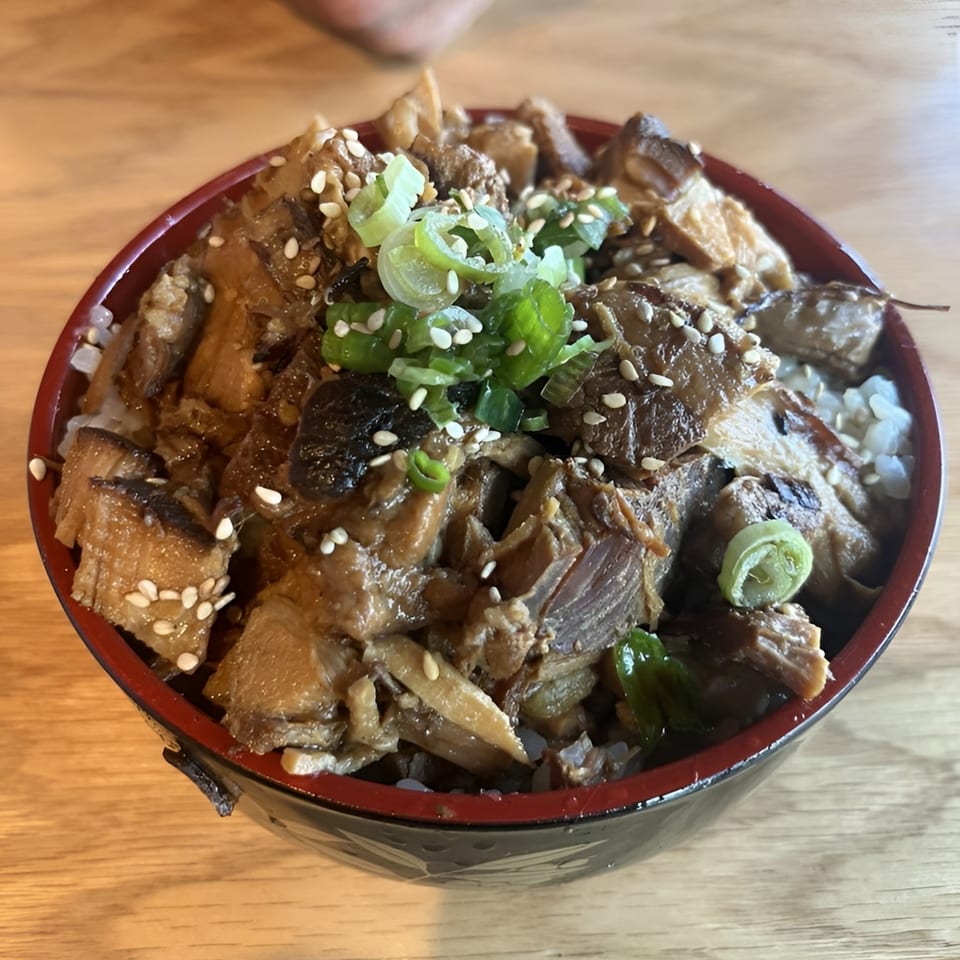 A close-up of a Japanese chashu donburi bowl with pork, green onions, and sesame seeds.