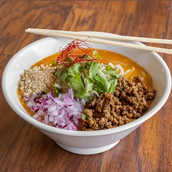A bowl of Takashi Ramen's tantanmen with ground pork, red onions, cilantro, and chili threads.