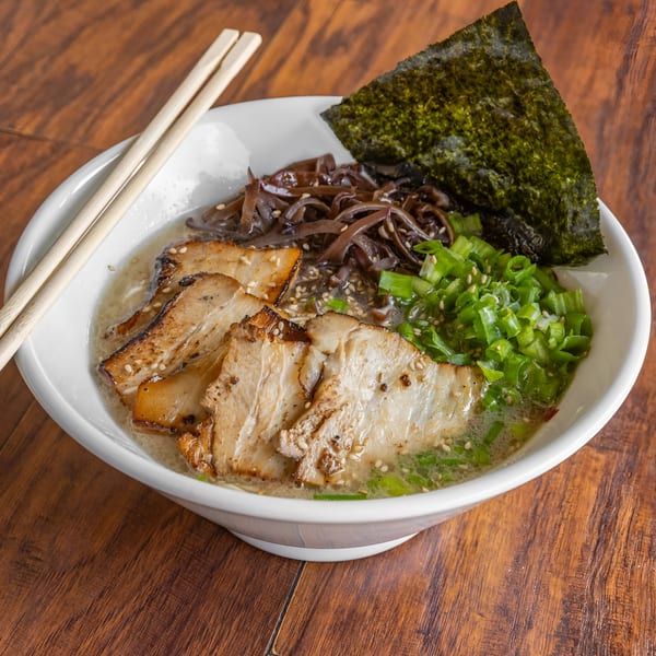 A bowl of Takashi Ramen with pork, green onions, wood ear mushrooms, and nori, with chopsticks.